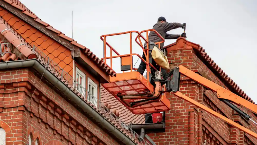 Worker on lift repairing brick roofline on a multi-story building